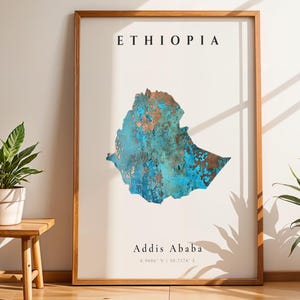 Puede incluir: Un cuadro enmarcado con un mapa de Etiopía con un diseño azul y cobrizo. La palabra "ETHIOPIA" está impresa en la parte superior y "Addis Ababa" en la inferior. Dos plantas en macetas flanquean la obra de arte.