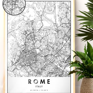 Può includere: Una mappa in bianco e nero incorniciata di Roma, Italia, con una planimetria dettagliata delle strade. La mappa include un inserto circolare che mostra una sezione ingrandita. Il nome della città e le coordinate sono visualizzati in basso. La cornice è di colore chiaro e una pianta in un vaso intrecciato è sullo sfondo.