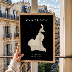 May include: A framed print featuring a map of Cameroon against a black background. The country's outline is in a light, textured color, with the name "Cameroon" at the top and "Yaoundé" at the bottom. The frame is gold.