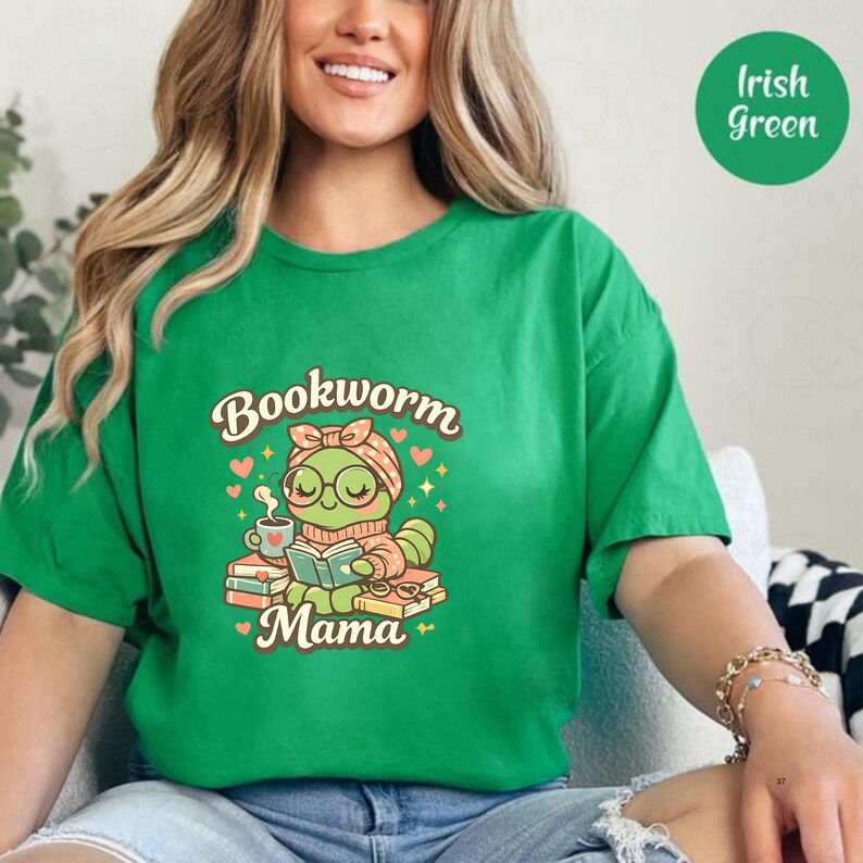 Op de afbeelding: Groen t-shirt met de tekst "Bookworm Mama" en een cartoon boekenwurm die een boek leest. De boekenwurm draagt een bril en een hoofdband. Het ontwerp bevat een kopje koffie en hartjes.