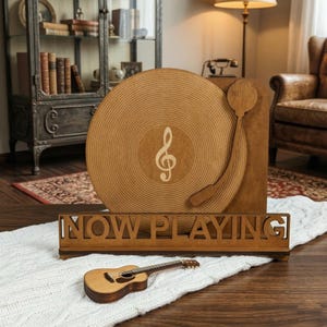 May include: Wooden decorative record player with a treble clef design. The words "NOW PLAYING" are cut out of a wooden sign. A miniature acoustic guitar rests on a white knitted blanket.