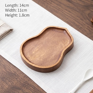Op de afbeelding: Een bruin houten dienblad met een gladde, organische, peervormige vorm. Het dienblad heeft een zichtbaar houtnerfpatroon en opstaande randen. De tekst op de afbeelding geeft de afmetingen aan: 14 cm lang, 11 cm breed en 1,8 cm hoog.