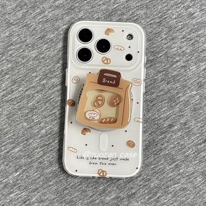 Puede incluir: Una funda de teléfono blanca con un diseño temático de pan. La funda presenta una bolsa de papel marrón con varios productos de panadería, incluyendo un pretzel y un cruasán. El texto "Bread" está en la bolsa, y también está presente la frase "Life is like bread just made from the oven".