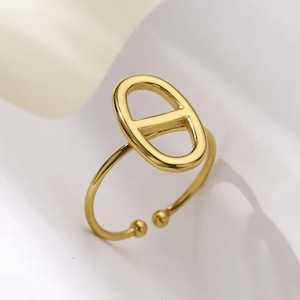 Peut inclure: Une bague réglable de couleur or avec un design ovale ouvert. La bague présente une finition lisse et polie et deux petits accents de boule aux extrémités ouvertes. La bague est posée sur un fond blanc doux.