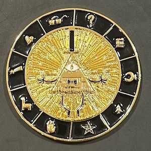 Könnte beinhalten: Ein runder, goldfarbener Metallpin mit schwarzem Rand. Der Pin zeigt ein zentrales Dreieck mit einem Auge, umgeben von radialen Linien. Der äußere Rand hat verschiedene Symbole. Der Pin hat eine glänzende, metallische Oberfläche.