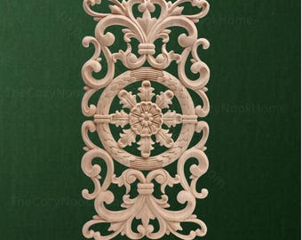 May include: A rectangular light-colored wooden carving featuring intricate symmetrical scrollwork and acanthus leaf patterns. The design centers on a circular medallion containing a floral motif, surrounded by elaborate swirling flourishes.
