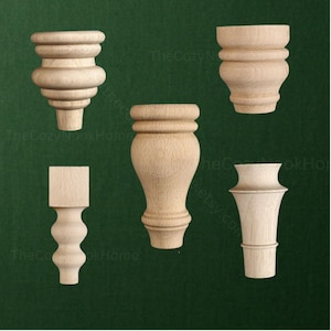 May include: Five unfinished light-colored wooden furniture legs in various turned shapes. The collection includes two rounded bun feet, one tall slender leg with a square top, one curved pedestal leg, and one tapered leg with a flared top section.