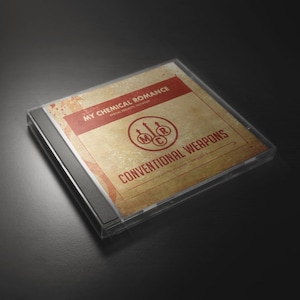Puede incluir: Un estuche de CD con el álbum "Conventional Weapons" de My Chemical Romance. La portada tiene una estética vintage con una pancarta roja y el logotipo de la banda. El estuche es transparente, mostrando el CD en su interior.