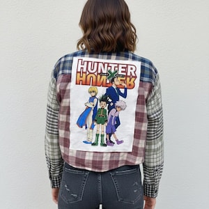 May include: Plaid button-up shirt with a graphic of anime characters and the text "HUNTER x HUNTER" on the back. The shirt features a mix of plaid patterns in shades of blue, burgundy, and gray. The graphic depicts four characters in various poses.