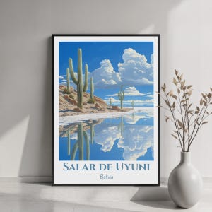Puede incluir: Una lámina de arte mural enmarcada que representa el Salar de Uyuni en Bolivia, con cactus verdes altos en una orilla rocosa reflejados en una superficie de agua azul clara bajo un cielo brillante con nubes blancas. El texto Salar de Uyuni Bolivia está abajo.