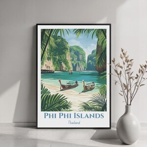 May include: A framed travel poster featuring a tropical landscape of Phi Phi Islands, Thailand. The illustration shows turquoise water, sandy shores, limestone cliffs, and palm leaves framing two long-tail boats. Text reads Phi Phi Islands Thailand.