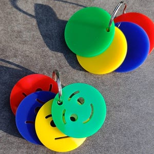 May include: Two metal rings each holding a collection of circular acrylic tags in red, blue, yellow, and green. One set features solid coloured discs, while the other set includes discs with laser-cut smiley face expressions and straight line mouths.