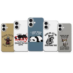 May include: Five phone cases with quirky designs. The cases display illustrations of a raccoon, a panda, a cat, and a creature holding a coffee cup. Each case has a unique quote, such as "I need money not a job." The cases are in various colours.