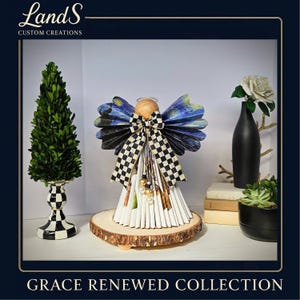 Puede incluir: Una figura de &aacute;ngel hecha a mano con alas de papel con un dise&ntilde;o de noche estrellada y un lazo a cuadros en blanco y negro. El &aacute;ngel est&aacute; sobre una base de madera, con el texto "Grace Renewed Collection". Los elementos decorativos incluyen un topiario, un jarr&oacute;n negro y una suculenta.