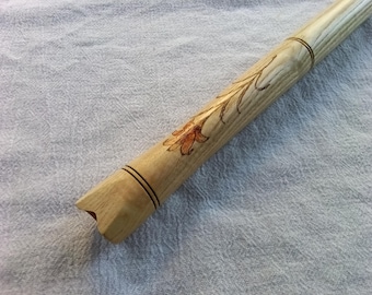 Puede incluir: Flauta de madera hecha a mano con un diseño floral. La flauta está hecha de madera de color claro y presenta un patrón de flores y hojas talladas. La flauta tiene dos bandas oscuras y un extremo con muescas.