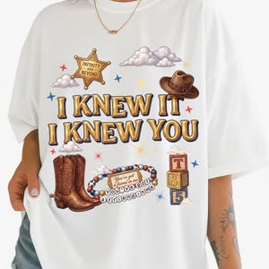 May include: A white t-shirt featuring the text I KNEW IT I KNEW YOU in gold lettering. The graphic includes a sheriff badge with the text INFINITY AND BEYOND, a brown cowboy hat, brown cowboy boots, a beaded bracelet, and three stacked blocks.