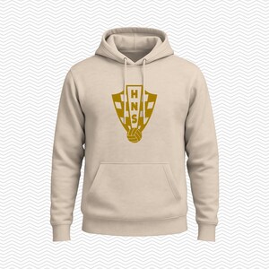 May include: A beige hooded sweatshirt featuring a gold-colored graphic on the chest. The graphic displays a shield with a checkered pattern, the letters HNS stacked vertically, and a soccer ball icon at the bottom. The hoodie has long sleeves.