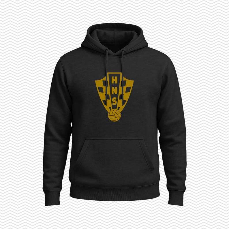 May include: A black hooded sweatshirt featuring a gold-colored shield emblem on the chest. The emblem displays a checkered pattern, the letters HNS stacked vertically, and a small soccer ball icon at the bottom. The hoodie includes a front pocket.