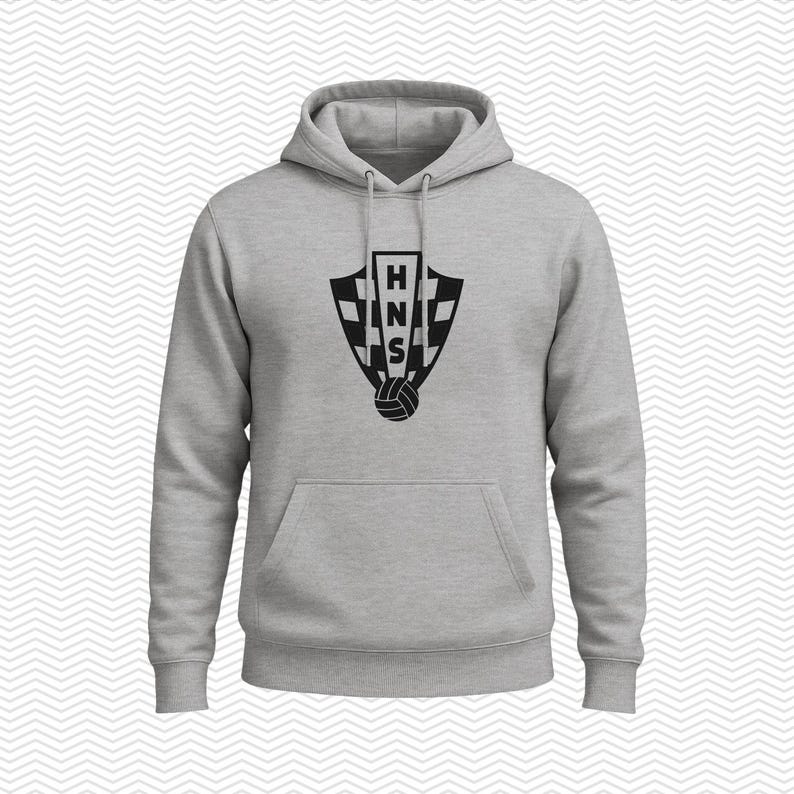 May include: A light gray hooded sweatshirt featuring a black graphic on the chest. The graphic displays a shield with a checkered pattern, the letters HNS stacked vertically in the center, and a soccer ball icon positioned at the bottom of the shield.