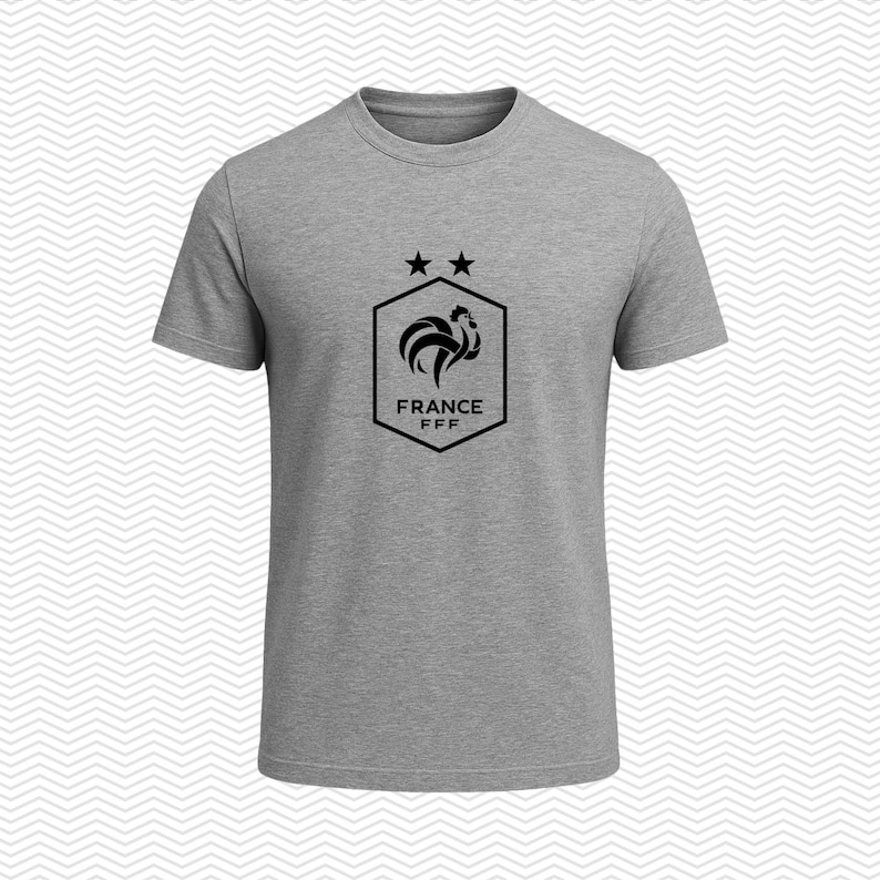 Puede incluir: Una camiseta gris jaspeado de manga corta con un gr&aacute;fico negro en el pecho. El gr&aacute;fico consiste en un borde hexagonal que contiene un gallo estilizado, dos estrellas sobre el hex&aacute;gono y el texto FRANCE FFF impreso dentro de la forma.