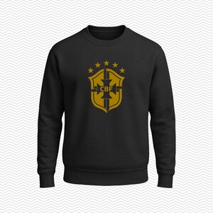 May include: A black long-sleeve crewneck sweatshirt featuring a gold-colored graphic on the chest. The graphic displays a shield emblem with the letters CBF in the center, topped by five small stars arranged in a horizontal arc above the shield.