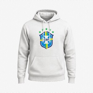 May include: A white hooded sweatshirt featuring a front kangaroo pocket and long sleeves. The center of the chest displays the blue, green, and yellow crest of the Brazilian Football Confederation with the letters CBF and five green stars above.
