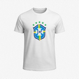 May include: A white short-sleeved t-shirt featuring the blue, green, and yellow CBF crest centered on the chest. The crest is topped with five green stars arranged in a semi-circle. The shirt has a classic crew neckline and a plain white back.