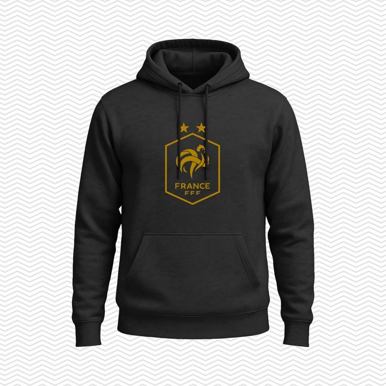Puede incluir: Una sudadera con capucha negra que presenta un gr&aacute;fico de color dorado en el pecho. El gr&aacute;fico muestra un emblema hexagonal con la silueta de un gallo, dos estrellas encima y el texto FRANCE FFF impreso en letras doradas dentro del hex&aacute;gono.