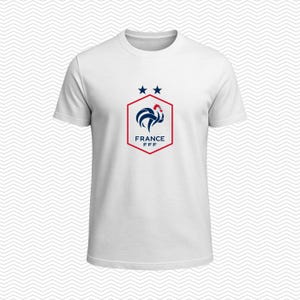 Puede incluir: Una camiseta blanca de manga corta con un gr&aacute;fico central de un gallo azul dentro de un hex&aacute;gono rojo. Sobre el hex&aacute;gono hay dos estrellas azules y, debajo del gallo, el texto FRANCE FFF en letras may&uacute;sculas de color azul.