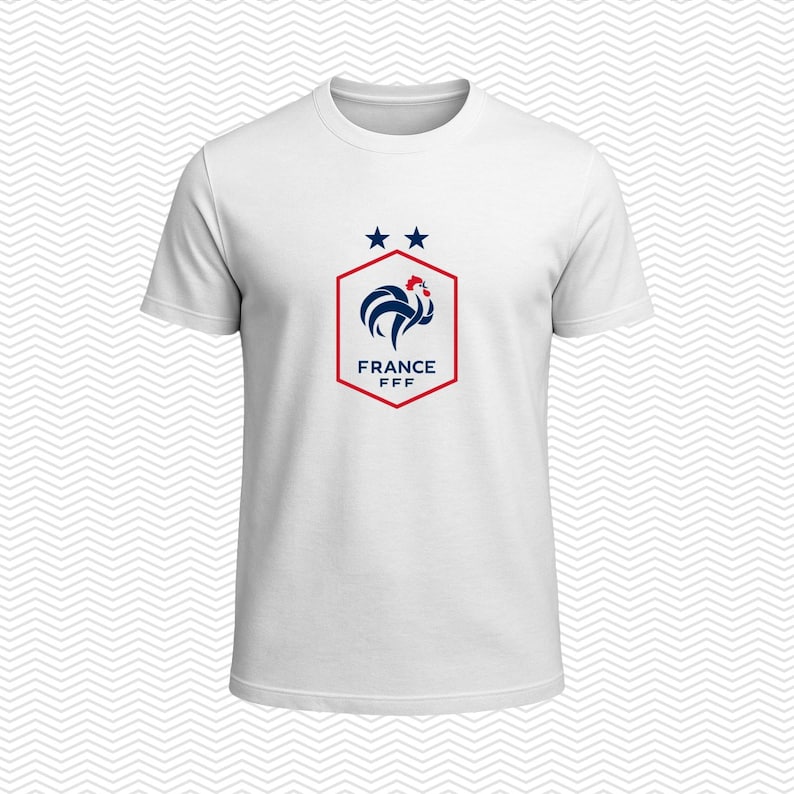 Puede incluir: Una camiseta blanca de manga corta con un gr&aacute;fico central de un gallo azul dentro de un hex&aacute;gono rojo. Sobre el hex&aacute;gono hay dos estrellas azules y, debajo del gallo, el texto FRANCE FFF en letras may&uacute;sculas de color azul.