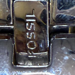 May include: Close-up of a silver watch clasp with the brand name "FOSSIL" and the number "15501" engraved on it. The clasp is rectangular and has a shiny, reflective surface.