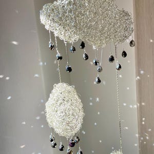 Könnte beinhalten: Handgefertigtes Mobile mit drei wolkenförmigen Skulpturen aus silbernem Draht. Jede Wolke hat tropfenförmige Kristallperlen. Das Mobile ist zum Aufhängen an der Decke konzipiert und verleiht jedem Raum einen Hauch von Eleganz.