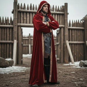 May include: A long, hooded red velvet cloak with gold trim. The cloak is worn over a medieval-style outfit, featuring a belt with a large buckle. The background includes a wooden fence and a dirt path, creating a historical or fantasy theme.