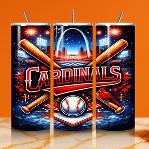 Pode incluir: Um copo com tema de beisebol com a palavra "Cardinals" em vermelho e branco. O design inclui bastões de beisebol cruzados, uma bola de beisebol, um cardeal vermelho e uma cena do estádio com o Arco Gateway.