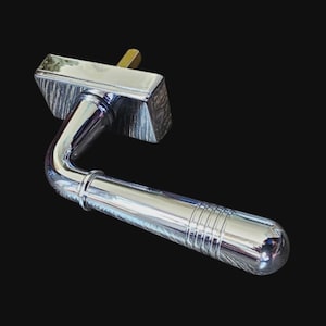May include: A chrome-finished door handle with a rectangular base and a curved lever. The handle has a polished, reflective surface and a cylindrical grip with etched horizontal lines. The base has a textured design.