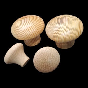 Pode incluir: Quatro puxadores em forma de cogumelo de madeira inacabada. Os puxadores são castanhos claros com grão de madeira visível. Dois puxadores estão em pé, dois estão deitados. Os puxadores têm um topo arredondado e uma base curta e cilíndrica.