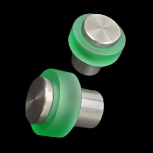 以下が含まれることがあります： モダンなデザインのキャビネットノブ2つ。各ノブは、円形のつや消しステンレス鋼の上面と半透明の緑色のベースが特徴です。ノブは銀色のステムに取り付けられており、黒い背景に配置されています。