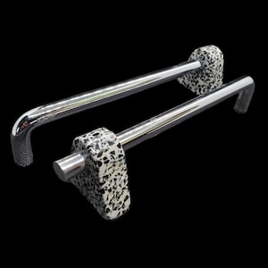 Può includere: Due maniglie per mobili con finitura cromata lucida e un design maculato bianco e nero sulle estremità. Le maniglie hanno un'impugnatura curva e una base rettangolare. Lo sfondo è nero.