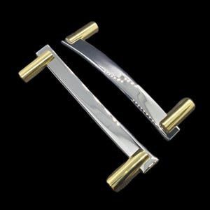 May include: Two polished silver cabinet handles with gold-colored end pieces. The handles have a sleek, modern design and are set against a black background. These handles are likely for kitchen or bathroom cabinets.