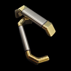 May include: Two cabinet pulls with a modern design. The handles are a combination of brushed silver and gold-toned metal. The ends of the pulls are square and gold, while the center is a silver bar. The pulls are set against a black background.