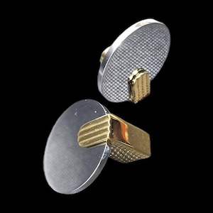 May include: A pair of silver and gold cufflinks. The oval silver faces have a textured pattern. The gold stems and backs are rectangular with a ridged design. The background is black.