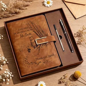 Puede incluir: Un cuaderno de aspecto de cuero marrón con un cierre de metal dorado, con una ilustración grabada de Winnie the Pooh y Piglet, el texto "NEVER FORGET THE DIFFERENCE YOU MAKE Mrs. Smith" y "Thank you, David", junto a un bolígrafo en una caja de regalo.