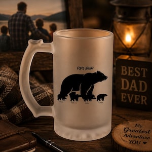 Puede incluir: Taza de cerveza de vidrio esmerilado con una silueta negra de un oso y tres cachorros, con la etiqueta "Papa Bear". Los nombres Linda, Rebecca, James y Connor están debajo. La taza tiene un asa grande y está sobre una superficie de madera.