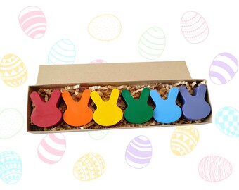 May include: A box of six bunny-shaped crayons in a rainbow of colors: red, orange, yellow, green, blue, and purple. The crayons are nestled in brown paper and surrounded by Easter egg illustrations.