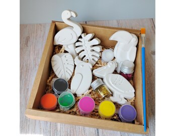 May include: A craft kit in a cardboard box, featuring unpainted plaster figurines of a flamingo, toucan, and tropical leaves. Includes paint pots in various colors, glitter, and a paintbrush. The kit is designed for creative projects.