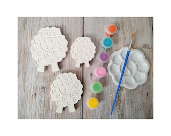 May include: A craft kit featuring three white sheep figurines, paint pots in various colors, a paint palette, and a paintbrush. The sheep have a curly wool design and smiling faces, perfect for a fun painting activity.