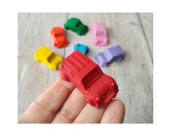 May include: A collection of colorful toy cars in red, green, yellow, orange, pink, blue, and purple. The red car is in focus, with the others slightly blurred in the background. The cars are small and appear to be made of plastic.