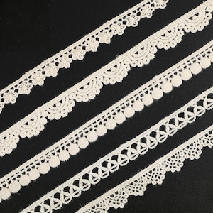 May include: An image showing several off-white lace trims with varied decorative edges. The trims are set diagonally against a black background. The lace designs include floral, scalloped, and geometric patterns, ideal for craft projects.