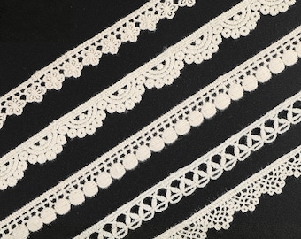 May include: Close-up of several off-white lace trims with different decorative edges. The trims are arranged diagonally against a black background. The lace designs include floral, scalloped, and geometric patterns, suitable for various craft projects.