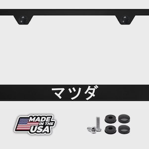 May include: Black license plate frame with the Japanese word "Mazda" in white lettering. Includes mounting hardware and a "Made in the USA" sticker. The frame is rectangular with rounded corners.